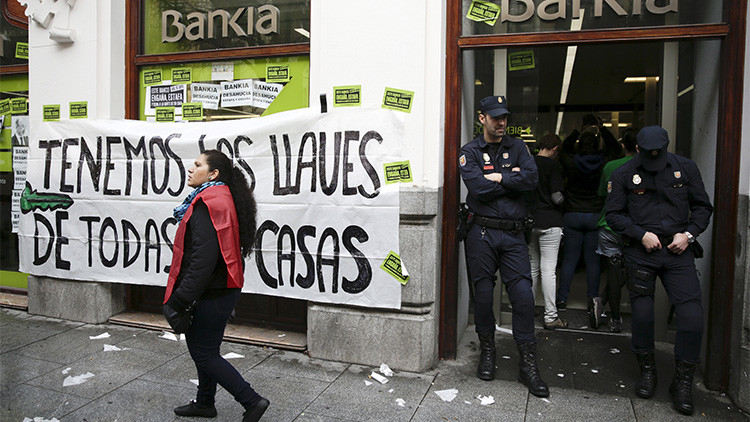 Una activista anti-desalojos pasa ante una pancarta mientras que unos policías bloquean la entrada de una sucursal bancaria de Bankia durante una protesta contra los desalojos en Madrid, España, el 11 de febrero de 2016.