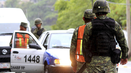 Soldados están de guardia mientras otros inspeccionan un vehículo en un puesto de control en Acapulco, México